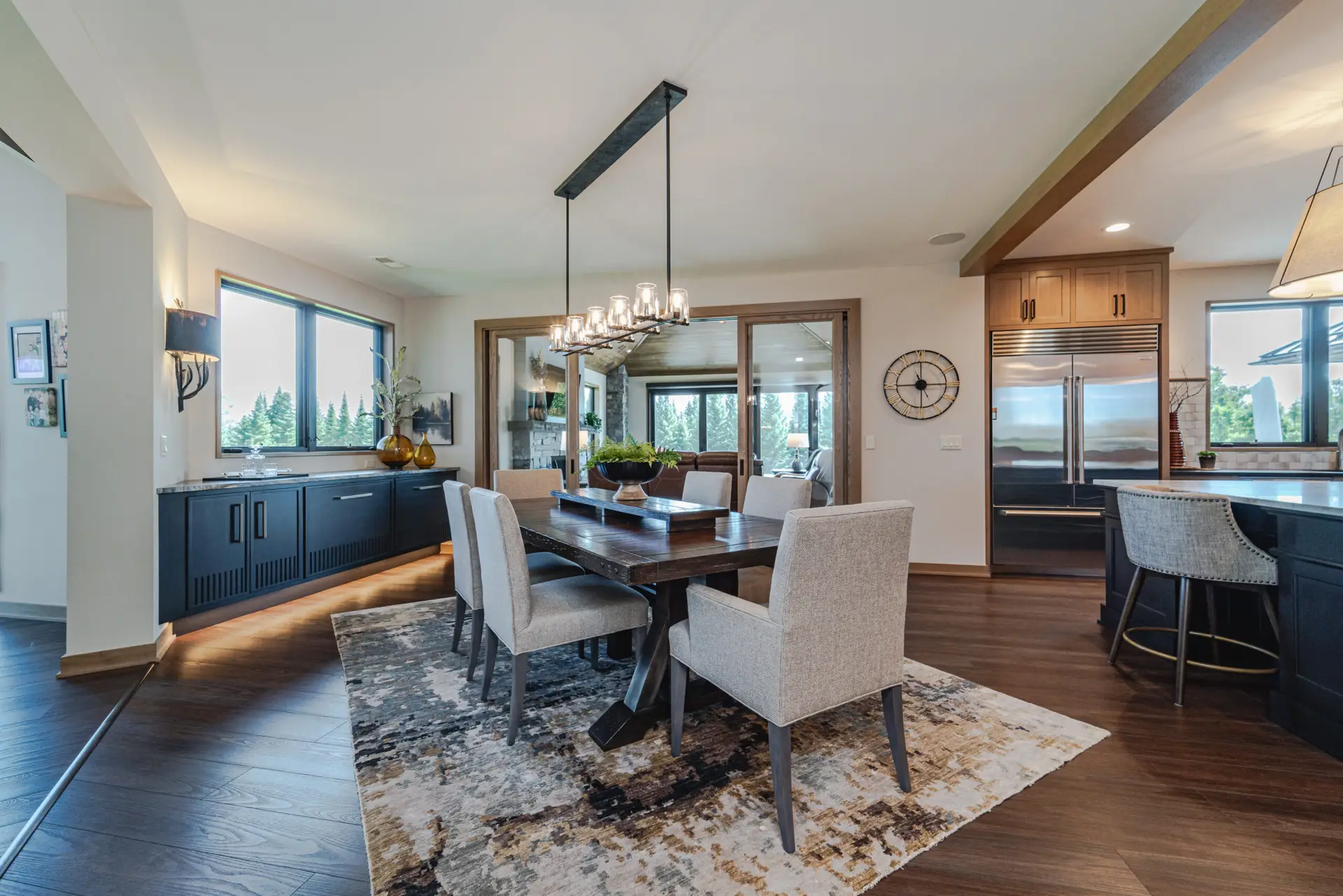 Open-concept dining area with a dark wood table, beige upholstered chairs, and a modern chandelier above the table.