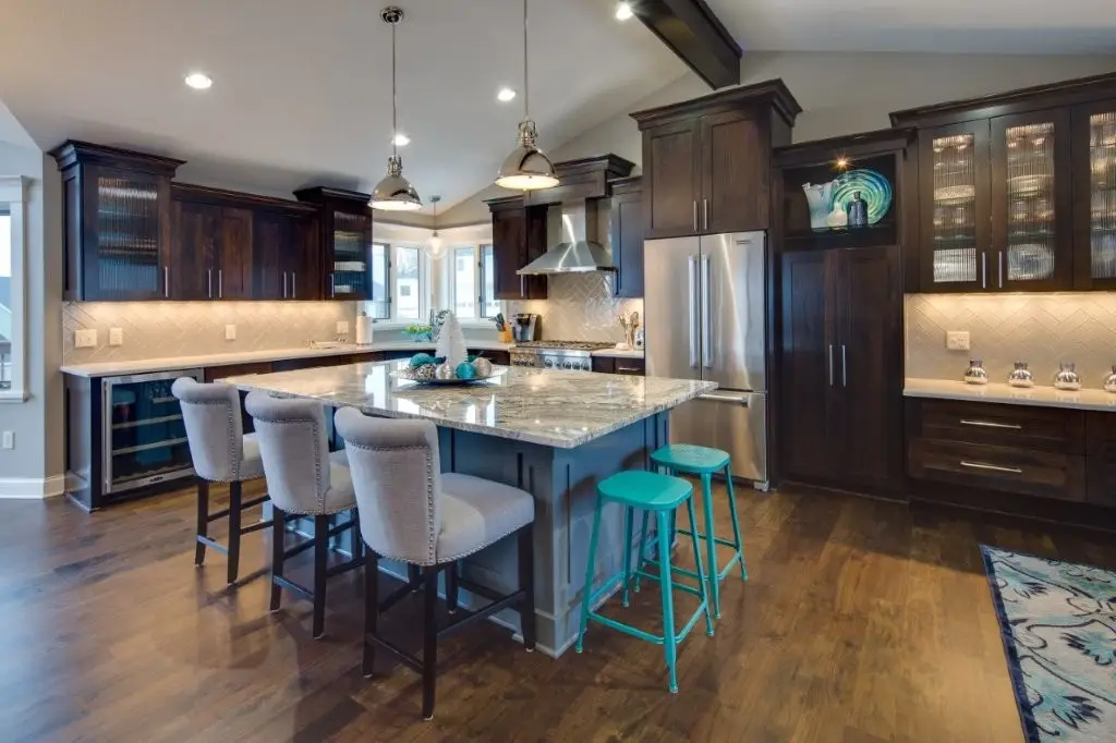 Modern kitchen with dark wood cabinets, a granite island, and stainless steel appliances with teal bar stools on one side.