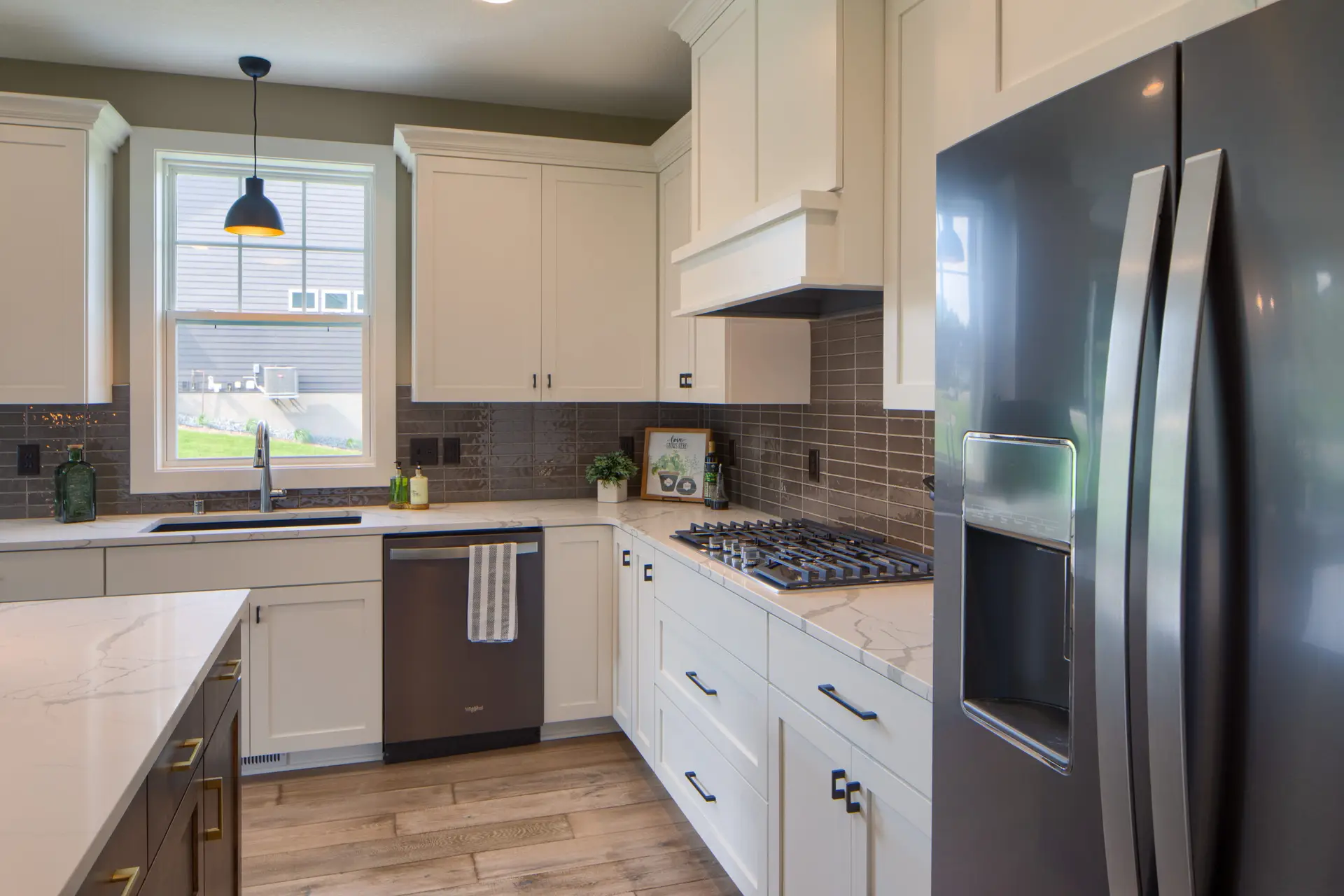 Modern kitchen with white cabinets, marble countertop, and gray tile backsplash under a pendant light near a windowed wall and stainless appliances