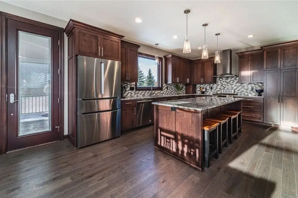 Modern kitchen with dark wood cabinets, stainless steel fridge, and a granite island with four stools.