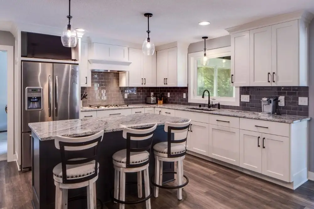 Modern kitchen with white Shaker cabinets, dark granite island, and three upholstered bar stools.