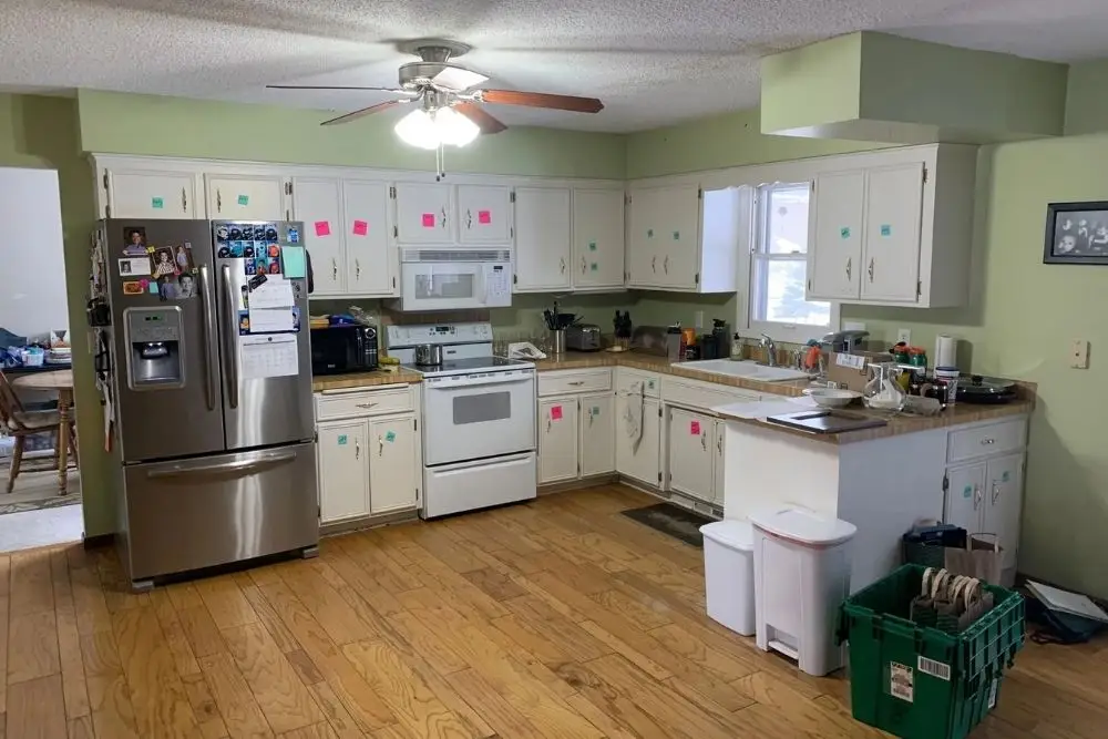 Bright green kitchen with white cabinets, stainless refrigerator, and pink sticky notes on cabinet doors.