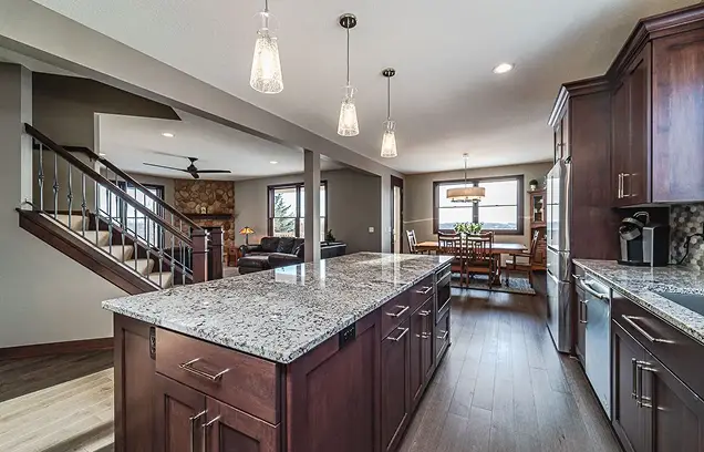 Open-concept kitchen with a granite island, dark wood cabinets, stainless appliances, and pendant lights, extending into a dining area and living room.