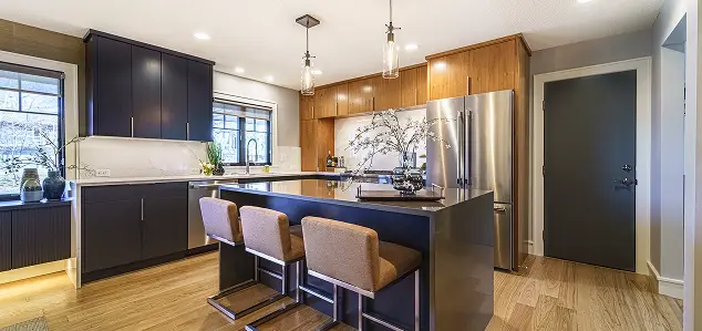 Modern kitchen with dark cabinets, stainless steel fridge, and a large island with three brown bar stools.