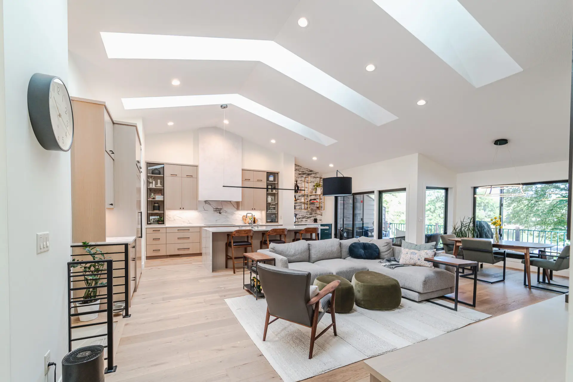 Open-concept living area with a bright kitchen, gray sectional, and skylight-lined ceiling letting in natural light
