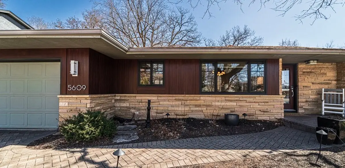 Front view of a single-story house with brick base and dark wood siding, two large windows, and an attached garage.