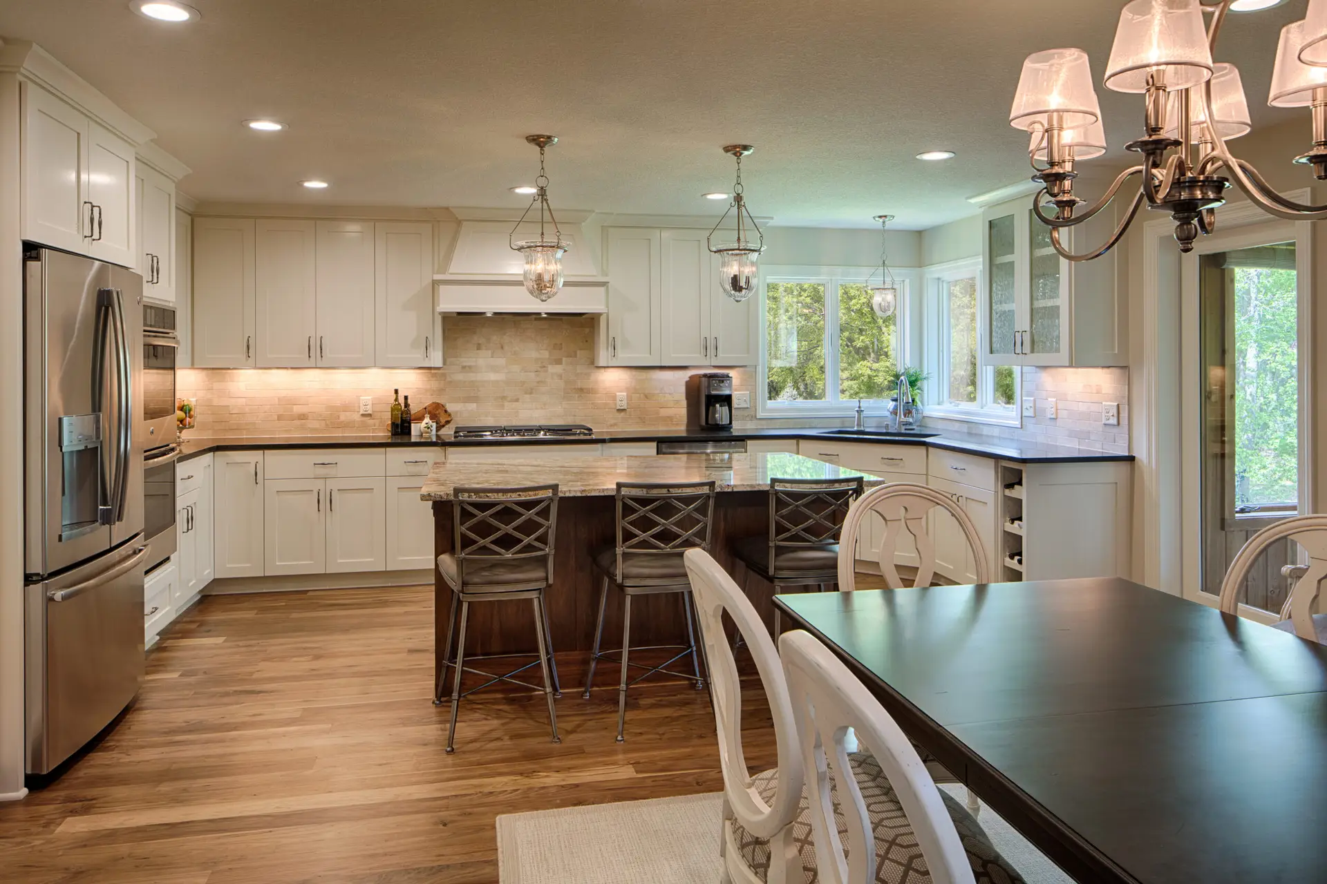 Bright, modern kitchen with white cabinets, a dark wood island, stainless steel appliances, and overhead glass pendant lights and a chandelier.