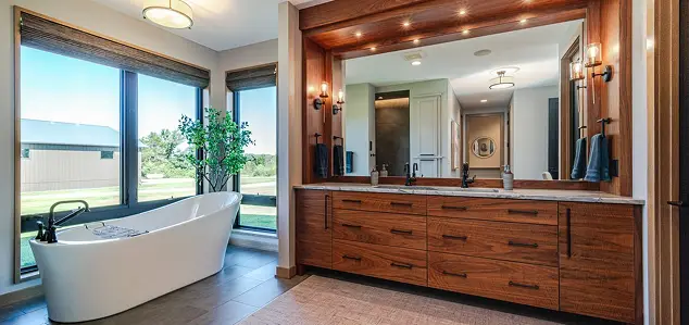 Luxurious bathroom with a white freestanding tub by large windows and a wooden double vanity with multiple drawers under a wide mirror.
